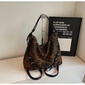 Detail of leopard print tote bag featuring a black leather strap and metal buckle accent