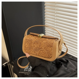 Detail of vintage embossed floral patterns and golden clasp on a light brown shoulder bag