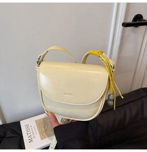 Détail du sac selle crème en similicuir lisse avec un pendentif cacahuète argenté