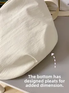 Detail des gefalteten Bodendesigns und des strukturierten Nylons der cremeweißen Umhängetasche
