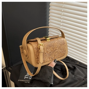 Detail of embossed floral patterns and golden lock on a vintage cylinder shoulder bag
