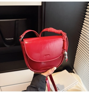 Détail du sac selle en cuir verni rouge avec gaufrage Lucky et breloque cacahuète