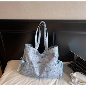 Détail du sac cabas à motif marbre avec nœuds bleus et poches avant sur un lit blanc