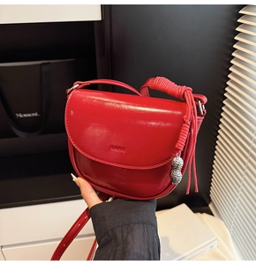 Détail d'un sac selle en cuir verni rouge avec pendentif cacahuète argenté et bandoulière tressée
