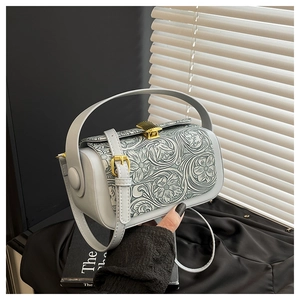 Detail of light blue box bag with floral embossing and gold hardware in soft lighting