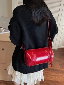 Glossy red cylinder shoulder bag in high-shine leather, worn by model in a stylish setting