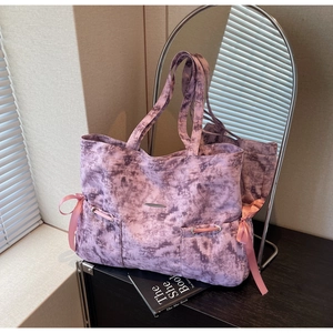 Détail du cabas en toile tie-dye violet avec des nœuds en satin rose et pièce métallique