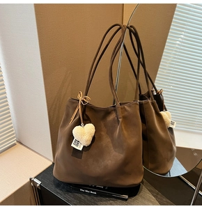 Detail of dark brown matte tote bag with heart plush charm on a wooden shelf