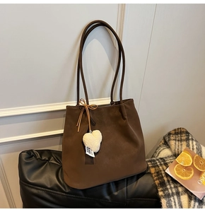 Detail of dark brown matte tote bag with plush heart pendant and bow tie strap design