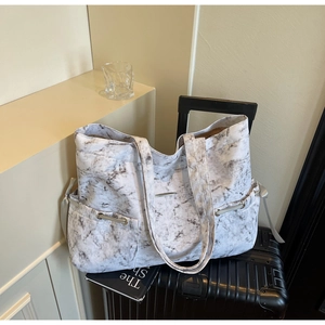 Détail du sac cabas à motif marbre avec cordon de serrage en ruban sur une valise