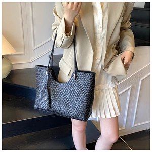 Détail d'un sac cabas tissé noir avec un petit porte-monnaie sur fond blanc minimaliste