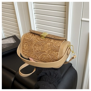 Detail of floral embossed vintage crossbody bag with gold wavy clasp and wide shoulder strap