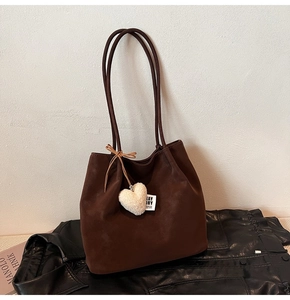 Detail of dark brown matte tote bag with a soft plush heart charm on black leather