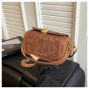 Detail of vintage brown leather bag featuring floral embossing and gold metal clasp