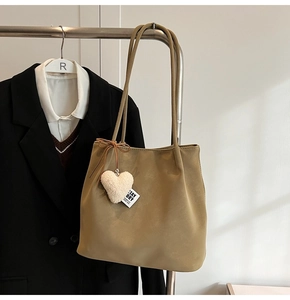 Detail of khaki suede tote bag featuring a white heart plush pendant and ribbon tag