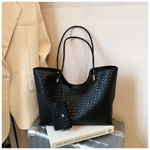Détail du sac cabas noir à texture tressée avec pochette sur valise argentée