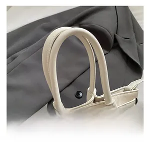 Gros plan sur la poignée cylindrique épaisse et la boucle métallique de ce sac seau crème