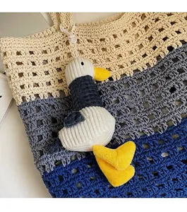 Detail of plush duck bag charm in blue and white corduroy on a striped crochet bag