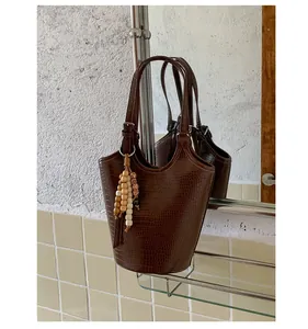 Detail of deep brown crocodile embossed bucket bag with ethnic beaded tassel charm