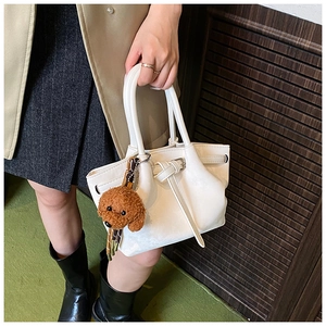 Détail d'un sac seau blanc avec boucle de ceinture et un porte-clé caniche en peluche