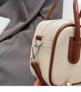 Detail of silver hardware and brown leather trim on cream woven shoulder bag