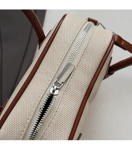 Close-up of a smooth silver metal zipper on a beige canvas bag with brown leather trim