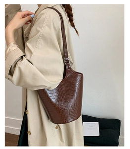Detail of dark brown crocodile-embossed bucket bag with silver metal buckles and sleek finish