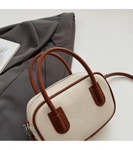 Detail view of woven cream Boston bag with brown leather handles on a grey blazer