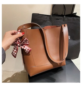 Detail of caramel brown leather tote bag featuring a red and white checkered scarf accent