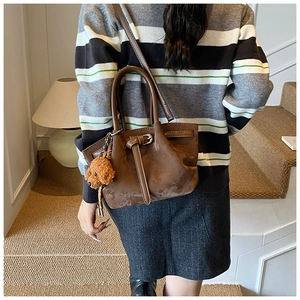 Sac seau marron en daim synthétique avec breloque ours porté dans un décor urbain