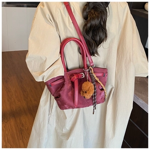 Détail du sac bandoulière bordeaux en tissu soyeux avec breloque ours sur manteau beige