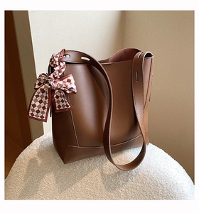 Detail of a brown leather tote bag with a checkered silk ribbon on a soft white base