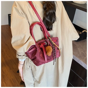Détail du sac seau bordeaux en daim avec poignée en cuir et breloque pelucheuse