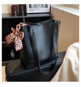 Black tote bag with a checkered silk ribbon detail on a decorative bookshelf background