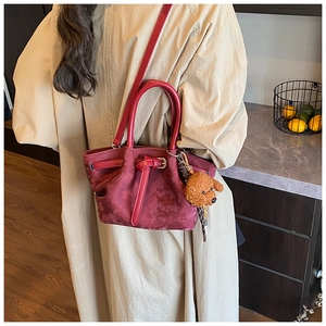 Détail du sac à bandoulière rouge vintage avec breloque peluche sur manteau beige