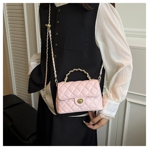 Détail d'un sac à main rose matelassé avec bandoulière en chaîne dorée porté par un mannequin