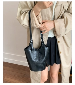 Close-up of black crocodile-embossed bucket bag worn with a beige trench coat