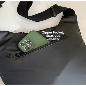 Detail view of the front zipper pocket on the black nylon crossbody bag with a phone inside