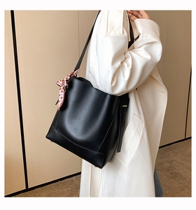 Detail shot of a black minimalist bucket bag with a decorative silk scarf on a model