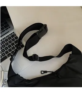 Close-up of a black crossbody bag with wide adjustable strap and plastic buckle on a desk