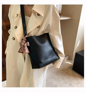 Detail of black leather bucket bag with gold studs and red checkered ribbon accessory