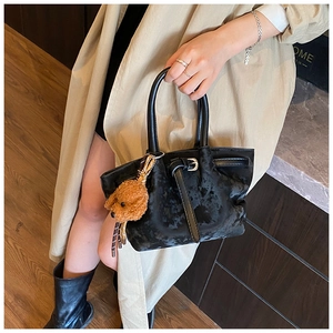 Détail d'un sac à main noir en daim avec sangle en cuir et breloque ours en peluche