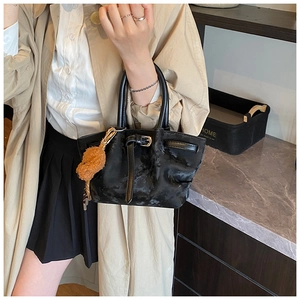 Détail d'un sac seau noir en peluche avec poignée en cuir et charmant petit ours
