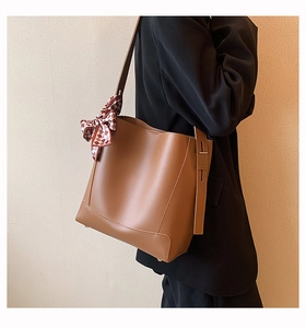 Detailed shot of brown bucket bag with red plaid bow ribbon on a textured wall background