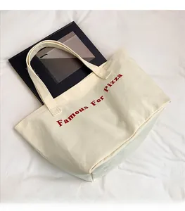 Dettaglio della borsa tote in tela color crema con stampa rossa Famous For Pizza e tracolla