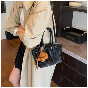 Détail du sac bandoulière en cuir noir avec boucles et adorable pendentif ours en peluche