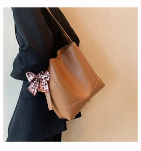 Brown leather bucket bag with plaid scarf detail shown on shoulder of model in black blazer