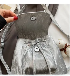 Detailed close-up of metallic silver backpack featuring magnetic buckle and drawstring closure