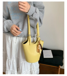 Detail of yellow crocodile embossed bucket bag with wooden bead charm and dual straps