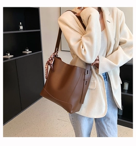 Brown leather bucket bag with silk scarf detail worn by a model in casual office attire